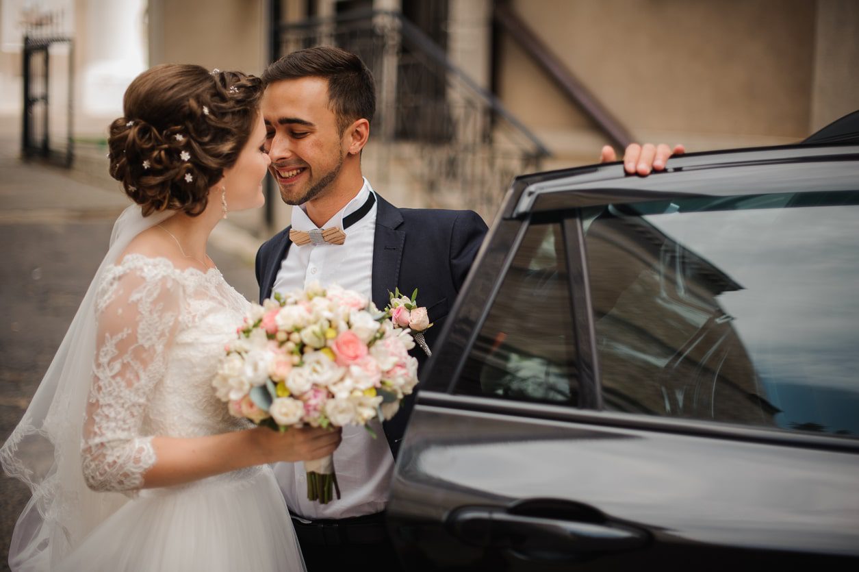 couple on wedding day posing with wedding car